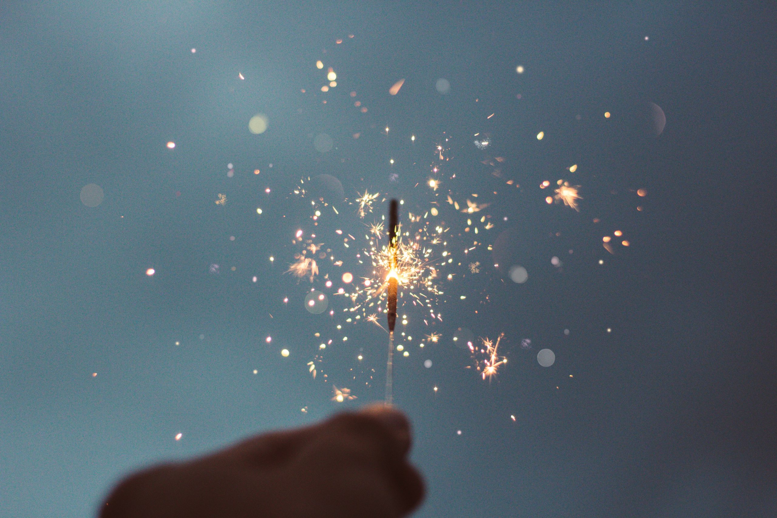 A hand holding a lit sparkler in front of a blue background.